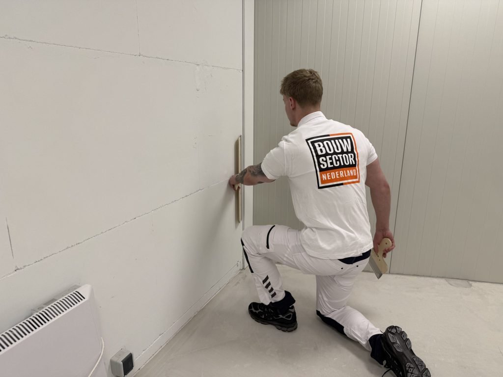 Stukadoor van Bouwsector Nederland knielt op een schone vloer en werkt de wand vlak boven de plint af